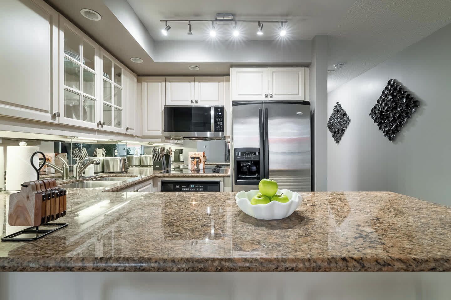 A modern kitchen with granite countertops, stainless steel appliances, and a bowl of green apples.