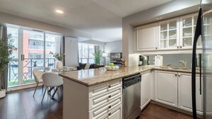 Uma cozinha moderna com ilha central, armários brancos, uma geladeira de aço inoxidável e um espaço de refeições com mesa e cadeiras de vidro.