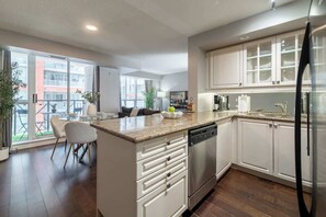 A modern kitchen with a central island, white cabinetry, a stainless steel refrigerator, and a dining area with a glass table and chairs.