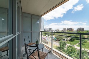 A balcony with a table and chairs, overlooking a cityscape with buildings and a grassy area. - Spacious Downtown Condo - Walk to CN Tower & More! | Parking Available (Toronto)