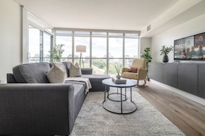 A modern living room with a grey sofa, a round coffee table, and a television on a cabinet. - Spacious Downtown Condo - Walk to CN Tower & More! | Parking Available (Toronto)