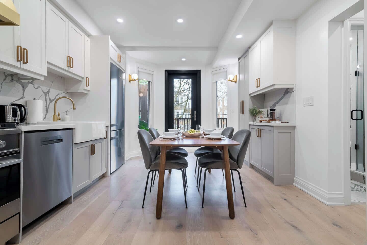 A modern kitchen with white cabinetry, a dining table with chairs, and a large window.