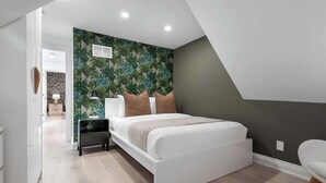 Un dormitorio moderno con cama, mesitas de noche y una pared con estampado de hojas.