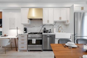 A modern kitchen with white cabinetry, stainless steel appliances, and a marble backsplash.