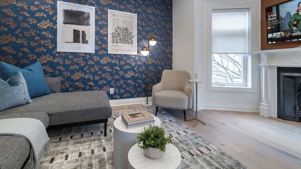 Una sala de estar con sofá, sillón y chimenea. Se observan obras de arte en las paredes y un televisor montado.