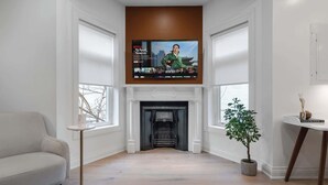 Una sala de estar con chimenea, un televisor montado encima, un sofá y una planta en maceta.