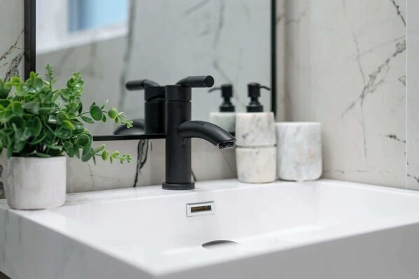 A bathroom with a white sink, black faucet, and a potted plant.