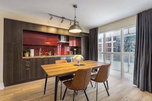 A modern kitchen with dark cabinets, a wooden dining table, and a large window with curtains. - Entertainment District 1BR Steps to CN Tower! | Parking Available (Toronto)