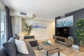 A modern living room with a sofa, a coffee table, a flat-screen TV, and artwork on the wall. - Entertainment District 1BR Steps to CN Tower! | Parking Available (Toronto)