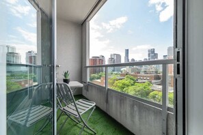 Ein Balkon mit Blick auf eine Stadtansicht, ein kleiner Tisch, ein Stuhl und ein Blumentopf.
