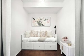 Ein helles Schlafzimmer mit einem Bett, einem Nachttisch, einer Lampe und einem an der Wand hängenden Bild.