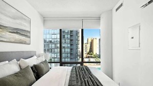 A modern hotel room with a large bed, a view of the city through floor-to-ceiling windows, and a minimalist design. - Downtown Financial District Gem Sleeps 5 55"TV (Toronto)