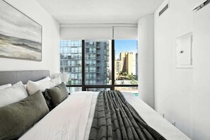 Ein modernes Hotelzimmer mit einem großen Bett, Blick auf die Stadt durch raumhohe Fenster und minimalistischem Design.