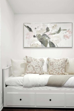Ein weißes Sofa mit Kissen in Blumenmuster und eine schlichte Wand mit einem gerahmten Blumenbild.