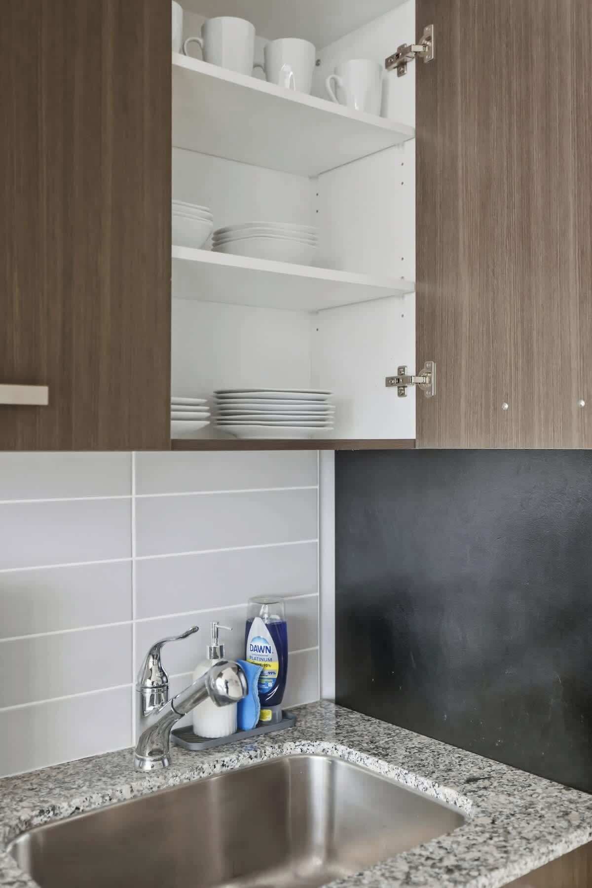 A kitchen with a granite countertop, stainless steel sink, and white tiled backsplash.