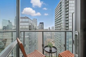 Ein Balkon mit Blick auf Stadtgebäude, ein Tisch mit einer Pflanze und zwei Stühle.