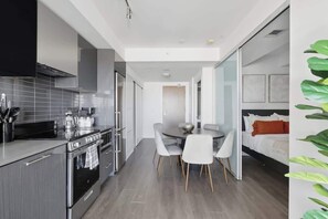 A modern kitchen with a dining area, a bed with a view, and a large plant. - Urban 2BR Suite near Yonge-Dundas | Private Balcony | Parking Available (Toronto)