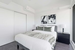 Ein modernes Schlafzimmer mit einem großen Bett, einem Nachttisch, einer Wandlampe und abstrakter Kunst an der Wand.