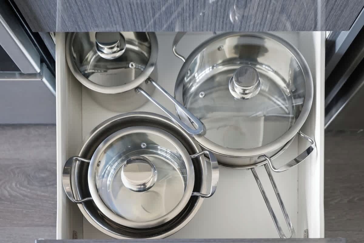 A stainless steel kitchen drawer with three pots and lids.