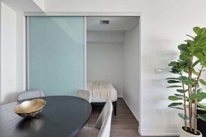 A modern room with a round table, a bench, a bed, and a potted plant. - Urban 2BR Suite near Yonge-Dundas | Private Balcony | Parking Available (Toronto)