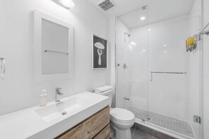 A modern bathroom with a white sink, wooden vanity, a toilet, and a glass-enclosed shower area. - Cozy 2BR Lower-Level Suite | Fast Transit! (Toronto)