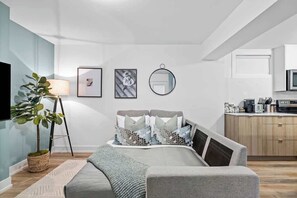A modern bedroom with a bed, bedside table, lamp, and a potted plant. - Cozy 2BR Lower-Level Suite | Fast Transit! (Toronto)