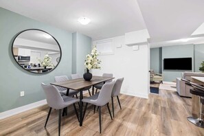 A modern living room with a dining area, a round mirror, and a flat-screen TV. - Cozy 2BR Lower-Level Suite | Fast Transit! (Toronto)