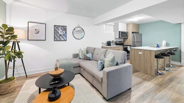 Una sala de estar moderna con un sofá, una mesa de centro y una pequeña zona de cocina con microondas y refrigerador.