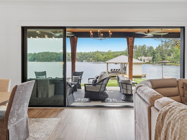 Een moderne woonkamer met een glazen deur die uitkomt op een terras met uitzicht op een meer.
