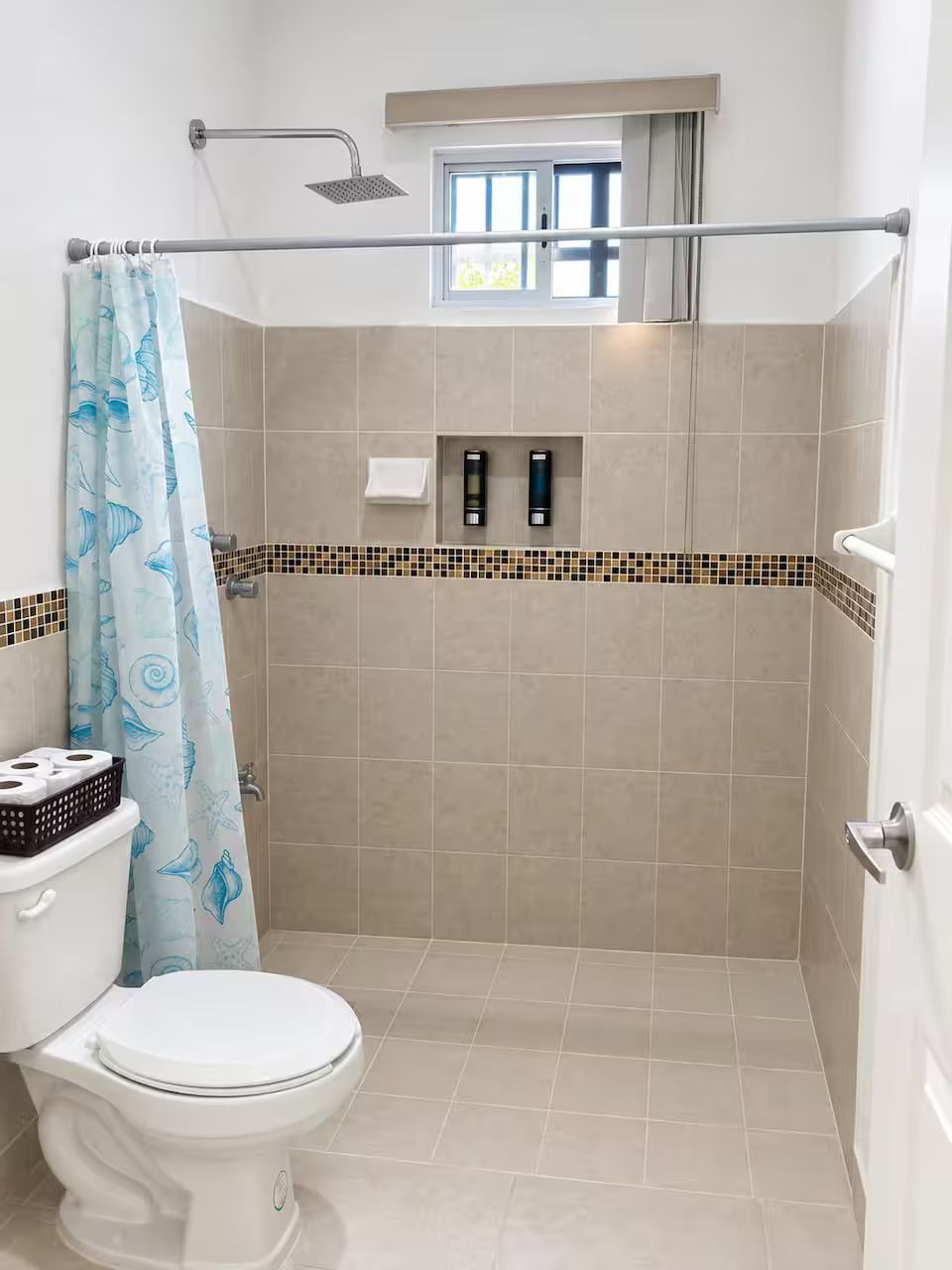 A bathroom with a shower, toilet, and a window above the shower.