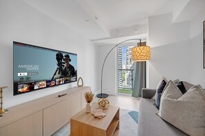Un soggiorno moderno con una televisione a schermo piatto che mostra una selezione di film, un divano, un tavolino da caffè e una lampada da terra.
