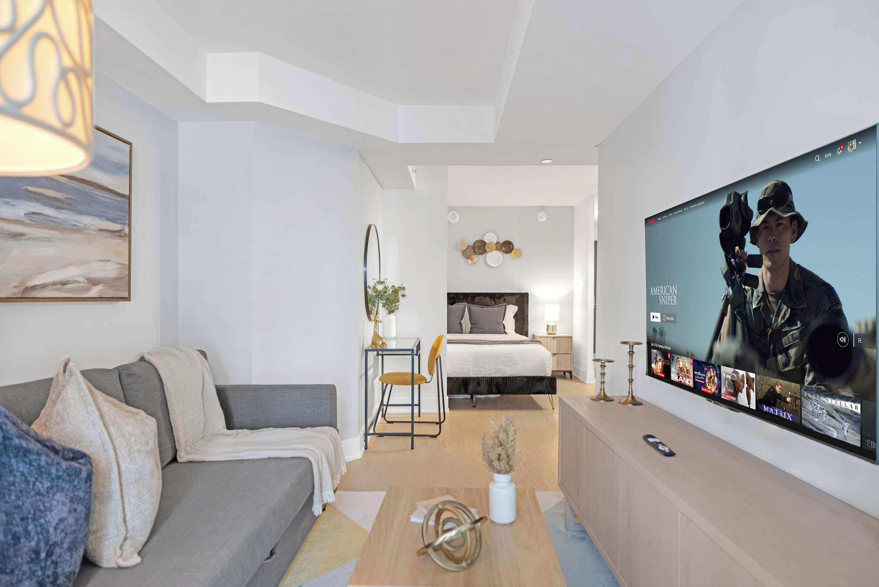 Una camera d'albergo moderna con un grande schermo televisivo, un divano, un letto e un tavolino con un vaso.