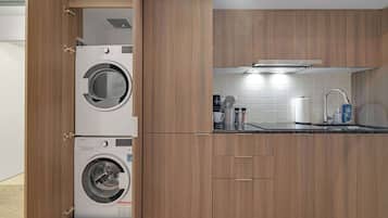 A compact kitchen with wooden cabinets, a built-in washing machine, a coffee maker, and a stainless steel sink.