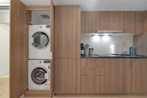 Una cucina compatta con mobili in legno, lavatrice integrata, macchina da caffè e lavello in acciaio inossidabile.