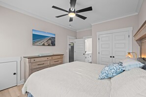 A bedroom with a bed, a ceiling fan, a dresser, a door, and a wall-mounted TV. - Driftwood Dreams at Ocean Lakes - w Golf Cart (Myrtle Beach)