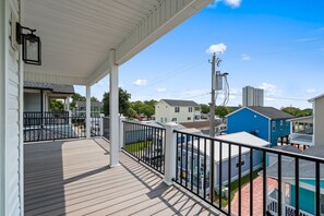A covered outdoor area with a wooden deck, a white railing, and a view of neighboring houses and a tall building in the background. - Driftwood Dreams at Ocean Lakes - w Golf Cart (Myrtle Beach)