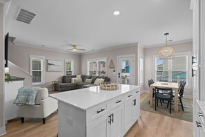 A modern kitchen with a central island, a dining area with a wooden table, and a living room with a sofa. - Driftwood Dreams at Ocean Lakes - w Golf Cart (Myrtle Beach)