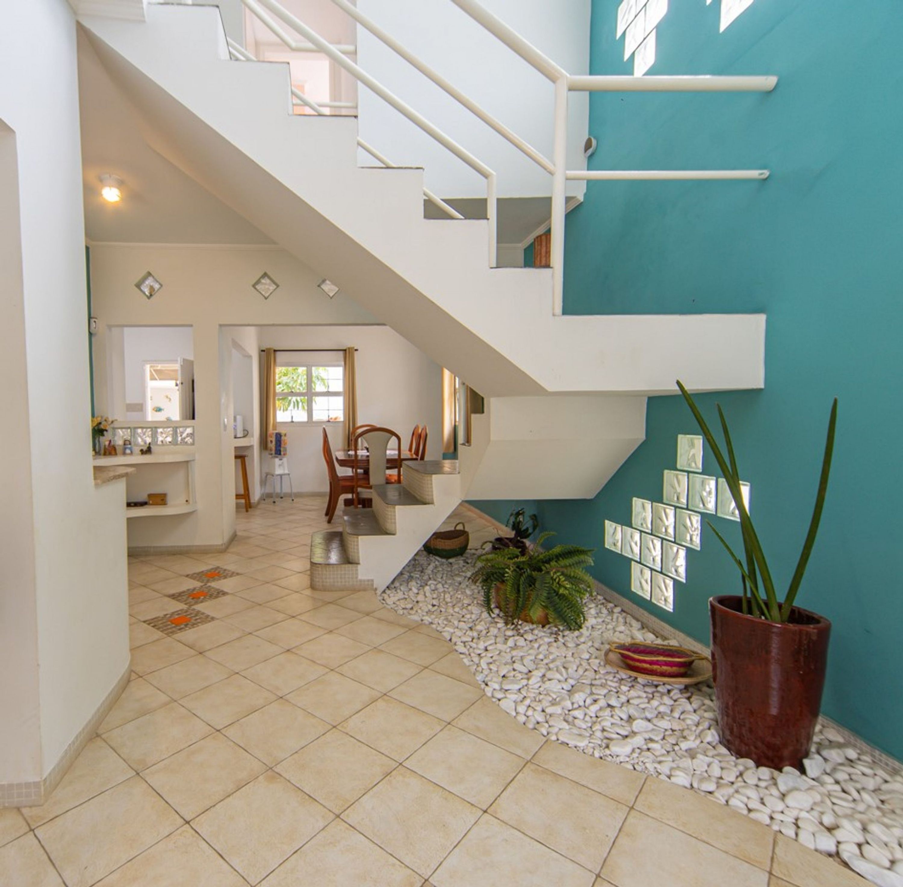 Um interior moderno com uma escada que dá para um andar superior, uma área de refeições com cadeiras e uma parede com quadros emoldurados.