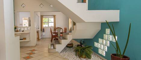 A modern interior with a staircase leading to an upper level, a dining area with chairs, and a wall with framed pictures.