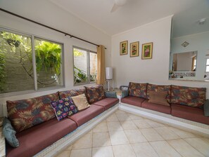 Uma sala de estar com sofá, radiador, espelho e quadros nas paredes.