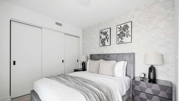 A bedroom with a bed, two bedside tables, a nightstand, a wardrobe, and two wall-mounted flower paintings.