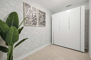 Ein Zimmer mit einem weißen Kleiderschrank, zwei floralen Bildern an der Wand und einer Topfpflanze.