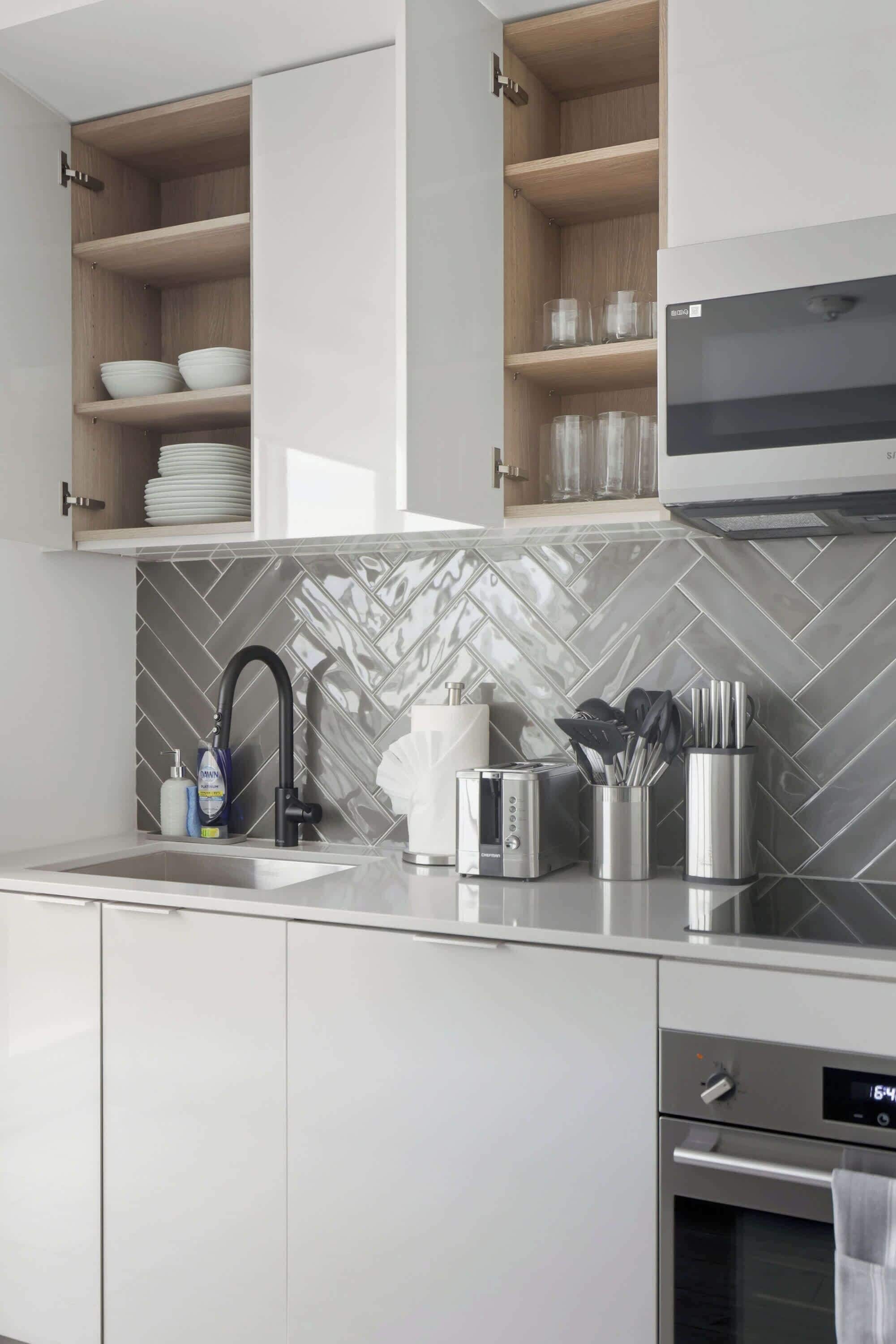 A modern kitchen with built-in cabinets, a microwave, a toaster, and a sink with a herringbone tile backsplash.