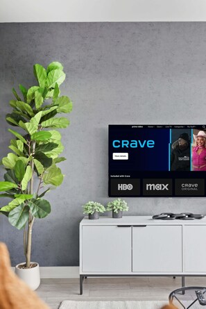 Un salon avec un téléviseur affichant le logo de « Crave », une plante en pot et un meuble blanc.