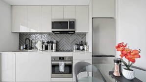 A modern kitchen with white cabinetry, a microwave, a coffee maker, and a refrigerator.