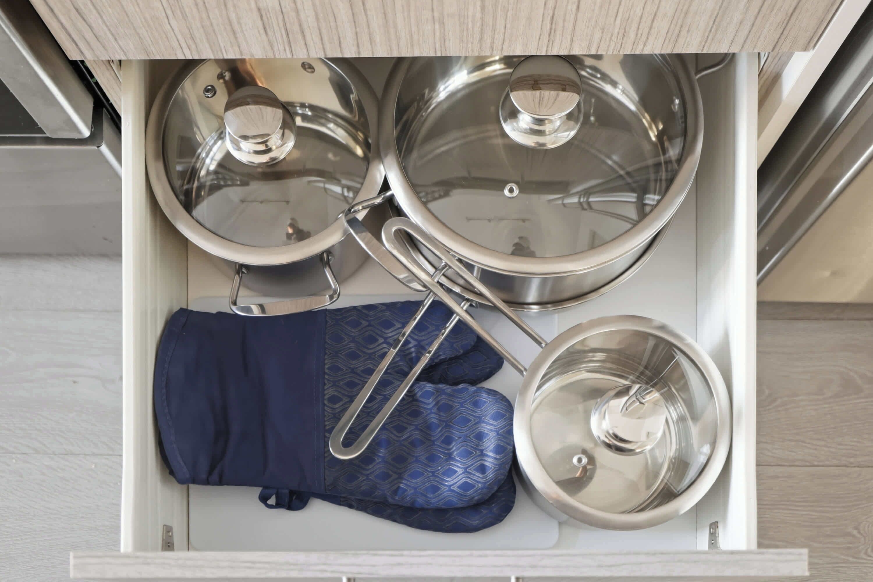 Un cajón de cocina con ollas, sartenes y guantes de horno.