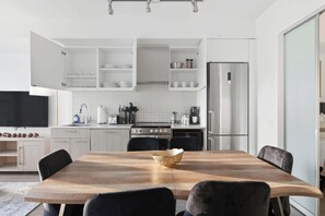 A modern kitchen with white cabinetry, a stainless steel refrigerator, and a dining area with a wooden table and chairs.