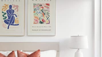 A bedroom with a bed, pillows, a nightstand, a lamp, and two framed artworks on the wall.