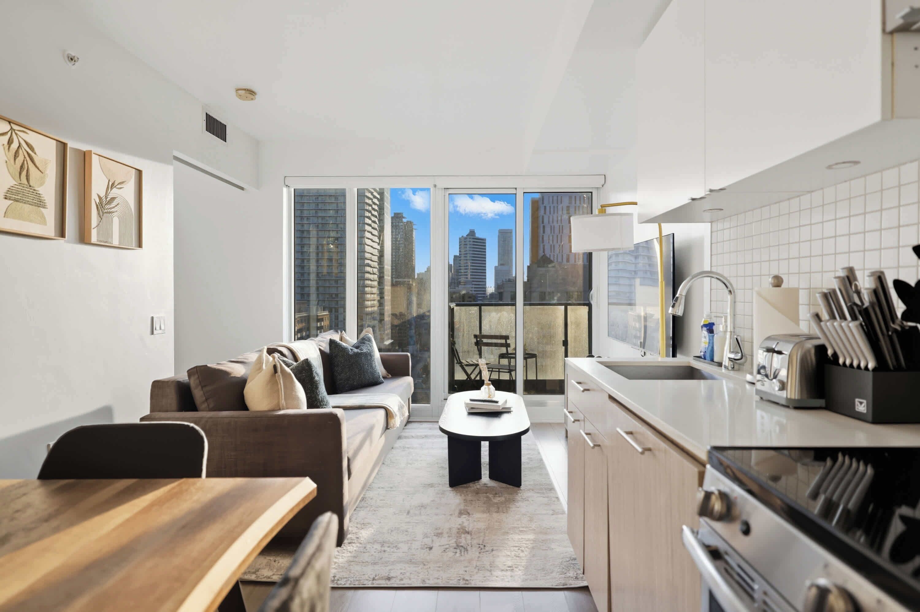 A modern apartment with a living area, kitchen, and large windows offering city views.