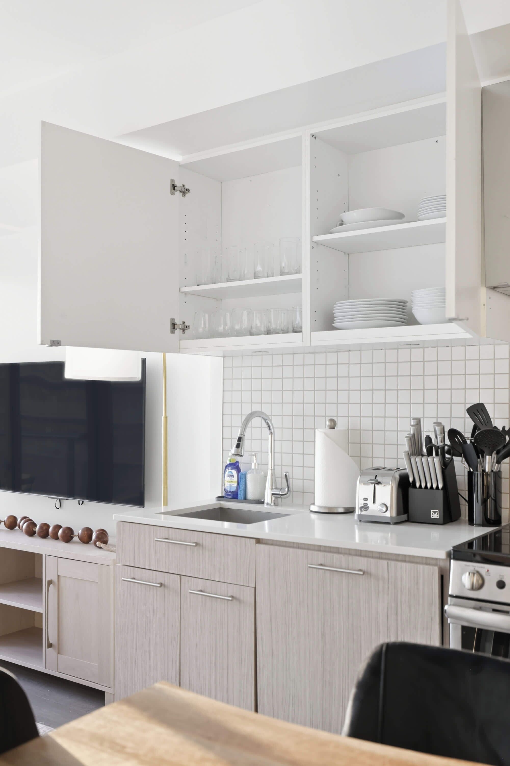 A modern kitchen with white cabinetry, a built-in dishwasher, a sink with a faucet, and a stove.